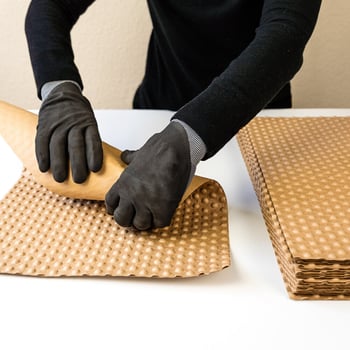 Hände packen einen Gegenstand mit PapairSheets ein, den vorgeschnittenen Bögen aus PapairWrap, der Luftpolsterfolie aus Papier.