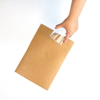 Eine Hand gießt Wasser auf PapairWrap Plus, die beschichtete Luftpolsterfolie aus Papier.